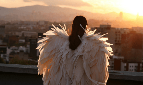Woman wearing white angel wings standing on a rooftop at sunrise, overlooking the city, symbolizing spiritual warfare, faith, and the inner battle between flesh and holiness.