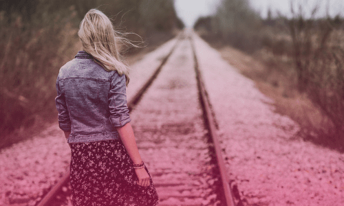 Woman standing still on train tracks, symbolizing feeling stuck in life and the need for change — 'A Bad Attitude Will Keep You Stuck, Here’s How to Keep Moving.
